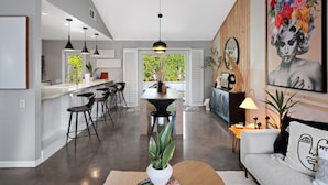 A modern kitchen with a central island, bar stools, pendant lighting, and a view of greenery outside. - 'Miles Away' A Desert Oasis - Palm Springs Style! (Palm Springs)