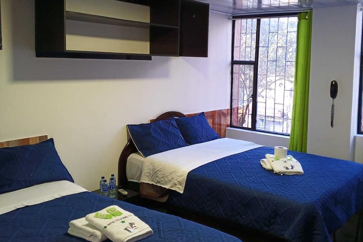 A hotel room with two beds, a window with a view, a shelf above the beds, and a telephone on the wall.