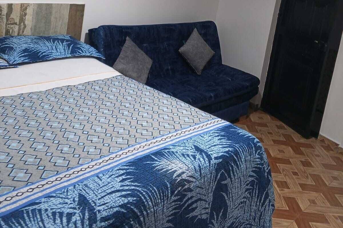 A bedroom with a bed, a blue sofa, a wall-mounted shelf, and a door.