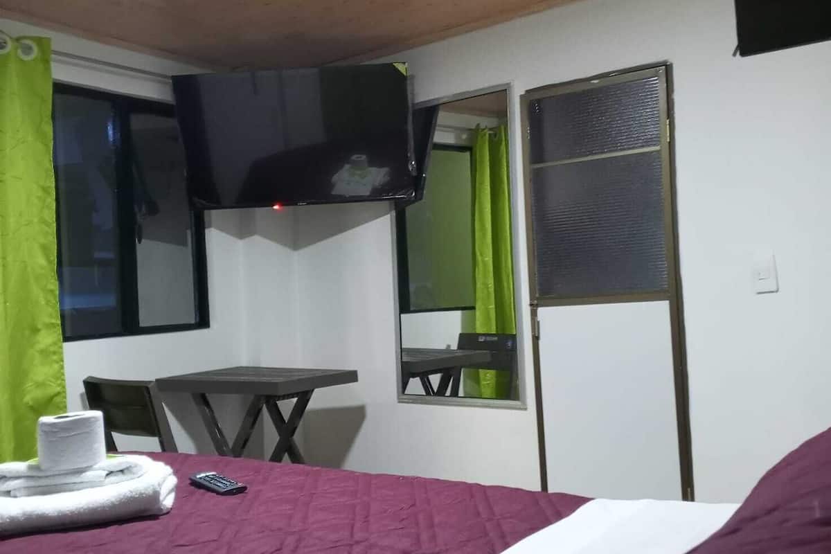 A small room with a bed, a desk, a chair, a window with a green curtain, and a mirror.
