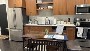 A modern kitchen with wooden cabinets, stainless steel appliances, a sink, and a dining area with stools. - Luxury Condo 5 minutes to downtown Traverse City, right next to TART trail! (Traverse City)