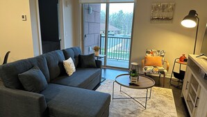 A modern living room with a grey sofa, a small round coffee table, and a TV stand. - Luxury Condo 5 minutes to downtown Traverse City, right next to TART trail! (Traverse City)