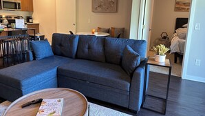 A modern living room with a sectional sofa, a coffee table, and a kitchen area in the background. - Luxury Condo 5 minutes to downtown Traverse City, right next to TART trail! (Traverse City)