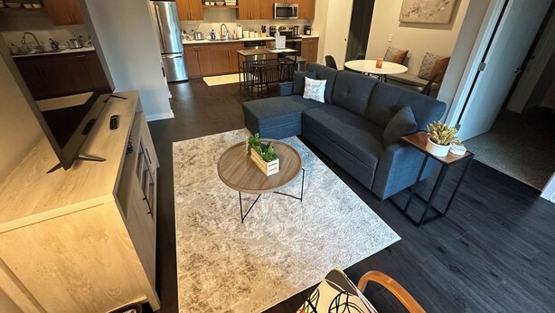 A modern open-plan living area with a sofa, coffee table, and kitchen in the background. - Luxury Condo 5 minutes to downtown Traverse City, right next to TART trail! (Traverse City)
