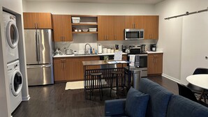 A modern kitchen with wooden cabinets, stainless steel appliances, and a dining area with a blue sofa. - Luxury Condo 5 minutes to downtown Traverse City, right next to TART trail! (Traverse City)