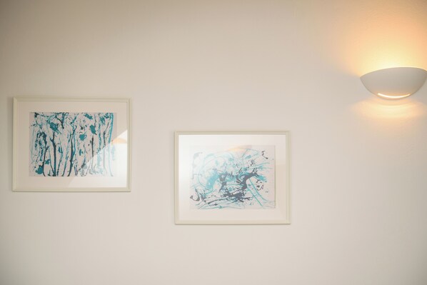 Two framed abstract paintings on a plain wall with a wall-mounted light fixture.
