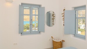 A bedroom with a bed, two windows, a mirror, and a wall-mounted shelf.