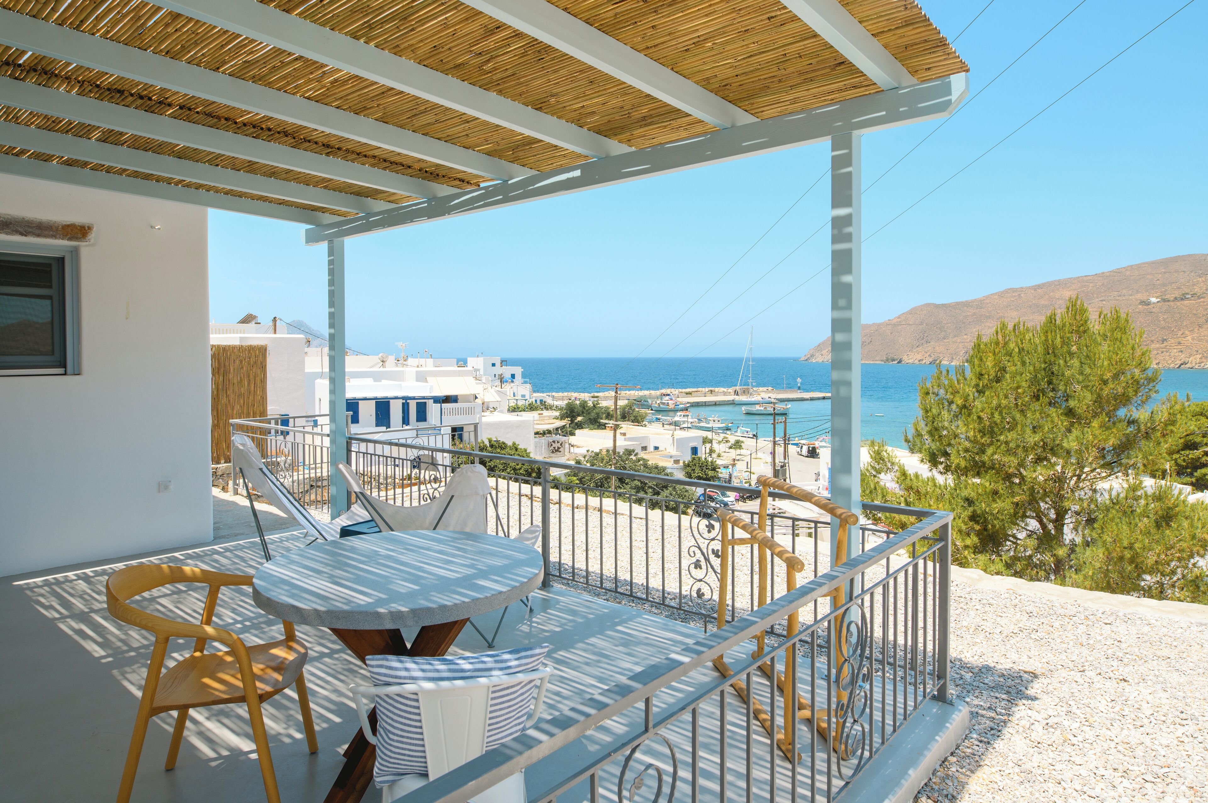 A balcony with a table and chairs, overlooking a coastal area with buildings and the sea.