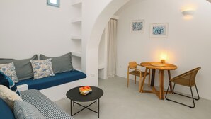 A modern living room with a blue sofa, a small round table with a book, and a wooden dining table with chairs.