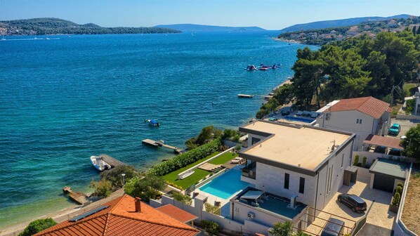 Una propiedad costera con piscina, un muelle con barcos y vista al mar.