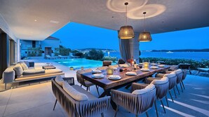 A modern outdoor dining area with a pool, overlooking a coastal view.
