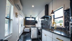 A modern kitchen with white cabinets, a black countertop, and a herringbone tile backsplash. - Contained In Gruene *Midnight* Spa/Outdoor Shower (New Braunfels)