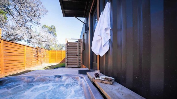 A hot tub area with a wooden deck, a wooden fence, and a white towel hanging on the wall. - Contained In Gruene *Midnight* Spa/Outdoor Shower (New Braunfels)