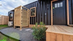 A modern building with a wooden deck, a black door, and a small window. - Contained In Gruene *Midnight* Spa/Outdoor Shower (New Braunfels)