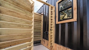 A wooden exterior with a black door and window, a concrete pathway, and a metal railing. - Contained In Gruene *Midnight* Spa/Outdoor Shower (New Braunfels)
