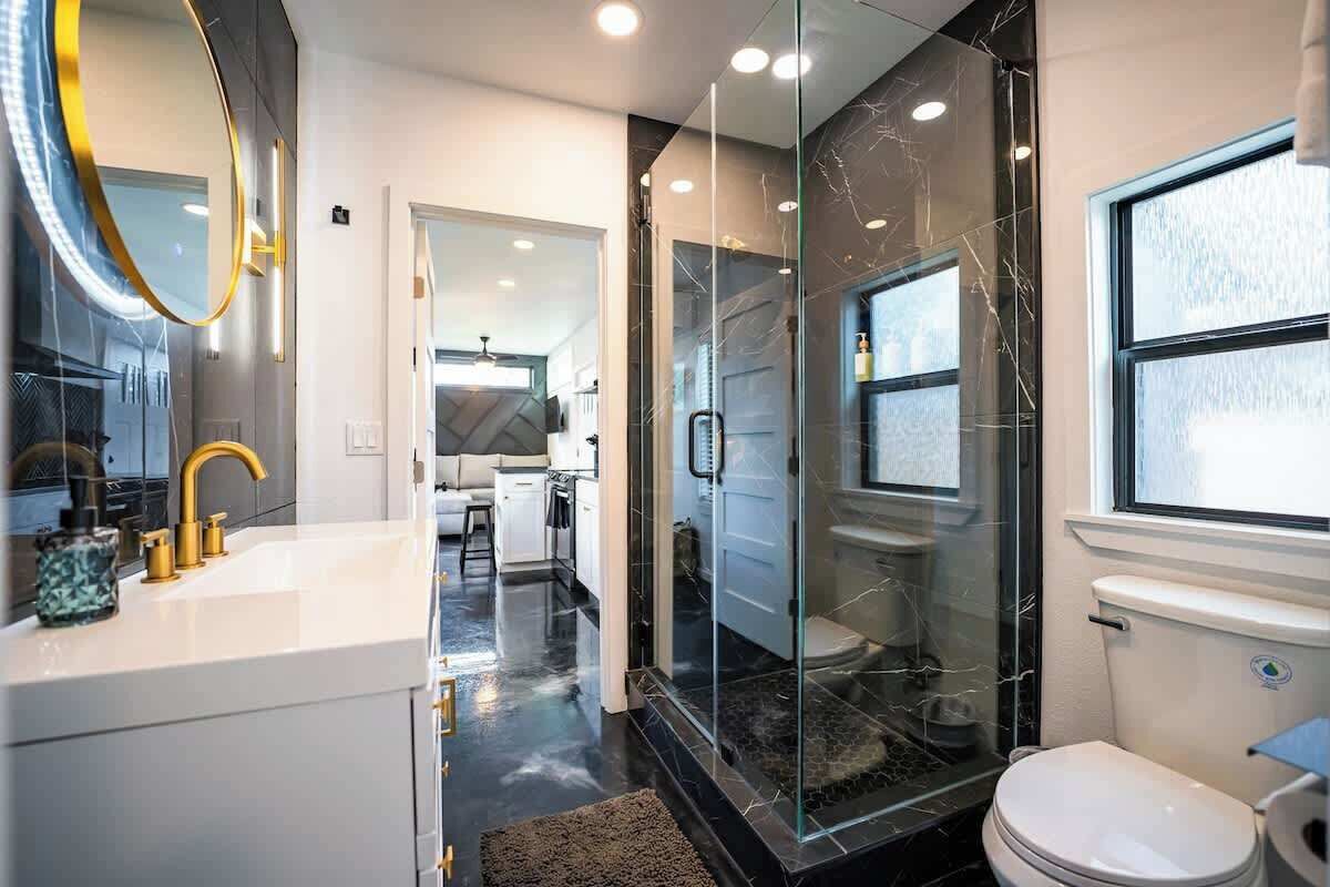 Une salle de bain moderne avec une douche à parois de verre, un lavabo blanc doté de robinetterie dorée et des toilettes.