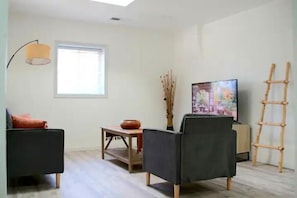 A modern living room with a sofa, a table with a bowl, a lamp, a TV, and a ladder. - Adobe Home with Modern Touch (Albuquerque)