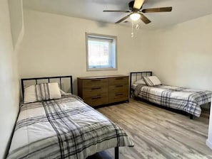 A bedroom with two beds, a dresser, a ceiling fan, and a window. - Adobe Home with Modern Touch (Albuquerque)