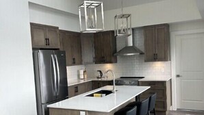 Une cuisine moderne dotée d’un îlot central, d’appareils électroménagers en acier inoxydable et de meubles de rangement en bois.