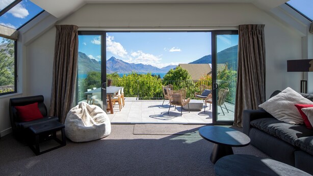 Ein modernes Wohnzimmer mit einer Couch, einem Couchtisch und einem Sitzsack. Ein Glastür öffnet sich zu einer Terrasse mit Tisch und Stühlen.