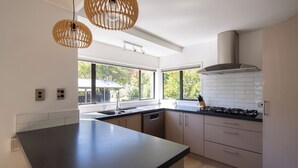 Eine moderne Küche mit einer großen Kochinsel, weißen Schränken und einem Gasherd. Zwei Pendelleuchten und ein Fenster sorgen für natürliches Licht.