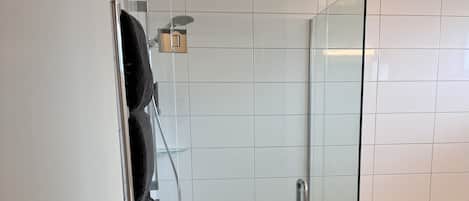 A modern bathroom with a glass shower enclosure, white tiled walls, and a dark floor.