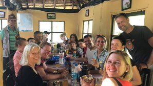 Un groupe de personnes est assis autour d’une table en bois dans une pièce rustique dont le toit est recouvert de chaume.