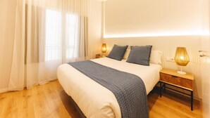 A modern hotel room with a large bed, two bedside lamps, a wooden nightstand, and sheer curtains.
