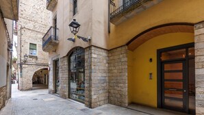 A narrow street with stone buildings, a shop with glass display windows, and a yellow building with a large door.