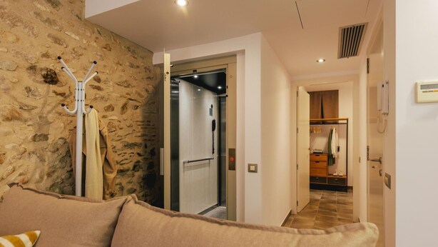 Un pasillo con pared de piedra, un perchero y una puerta que da a una habitación con un armario de madera y un teléfono.