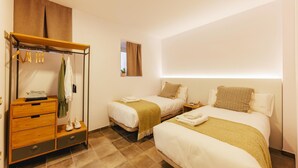 Habitación de hotel con dos camas, un armario de madera, una mesita y una ventana con cortinas.
