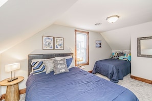 A bedroom with two beds, a nightstand, a lamp, and a window with blinds.