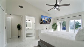 A modern bedroom with a large bed, a ceiling fan, a flat-screen TV, and a view of the outside through a sliding door.