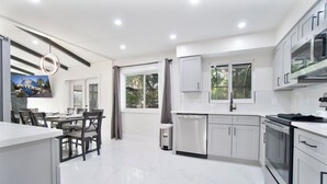A modern kitchen with white cabinetry, a dining area with a table and chairs, and a trash can.