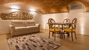 A cozy room with a brick ceiling, a stone wall, a sofa, a dining table with chairs, and a patterned rug. - Veronetta The Cellar (Verona)