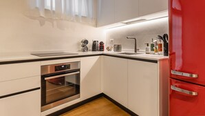 A modern kitchen with white cabinets, a red refrigerator, stainless steel appliances, and a window with sheer curtains. - Veronetta The Cellar (Verona)
