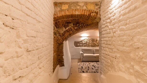 A narrow passageway with white brick walls leading to a cozy room with a sofa and a patterned rug. - Veronetta The Cellar (Verona)