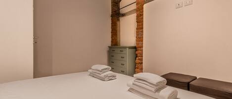 Un dormitorio con una cama, un aparador gris y una pared de ladrillo.