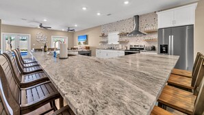 A modern kitchen with a large island, built-in appliances, and a dining area with wooden chairs.