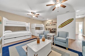 A hotel room with bunk beds, a desk, chairs, a ceiling fan, and a wall with surfboard decorations.