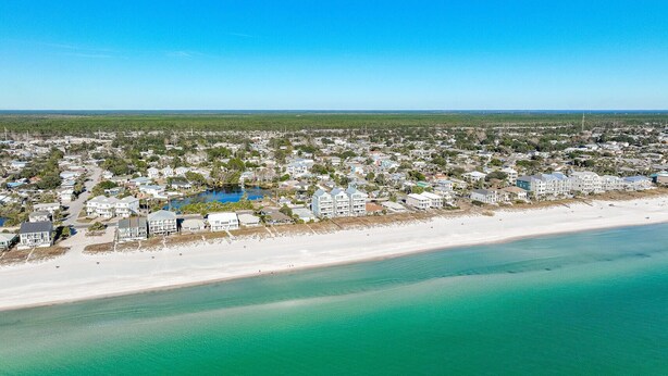 An aerial view of a coastal residential area with houses, a beach, and a clear blue sky.