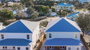 A residential area with two houses featuring blue roofs and white walls, a swimming pool, and a view of the ocean.