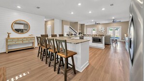 A modern kitchen with a central island, wooden chairs, and a refrigerator.