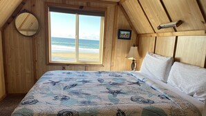 Et soveværelse med en stor seng, et vindue med udsigt til stranden, trævægge og et billede på væggen.