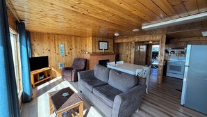 Et træpanelt interiør med sofa, fjernsyn, pejs og et tekøkken.