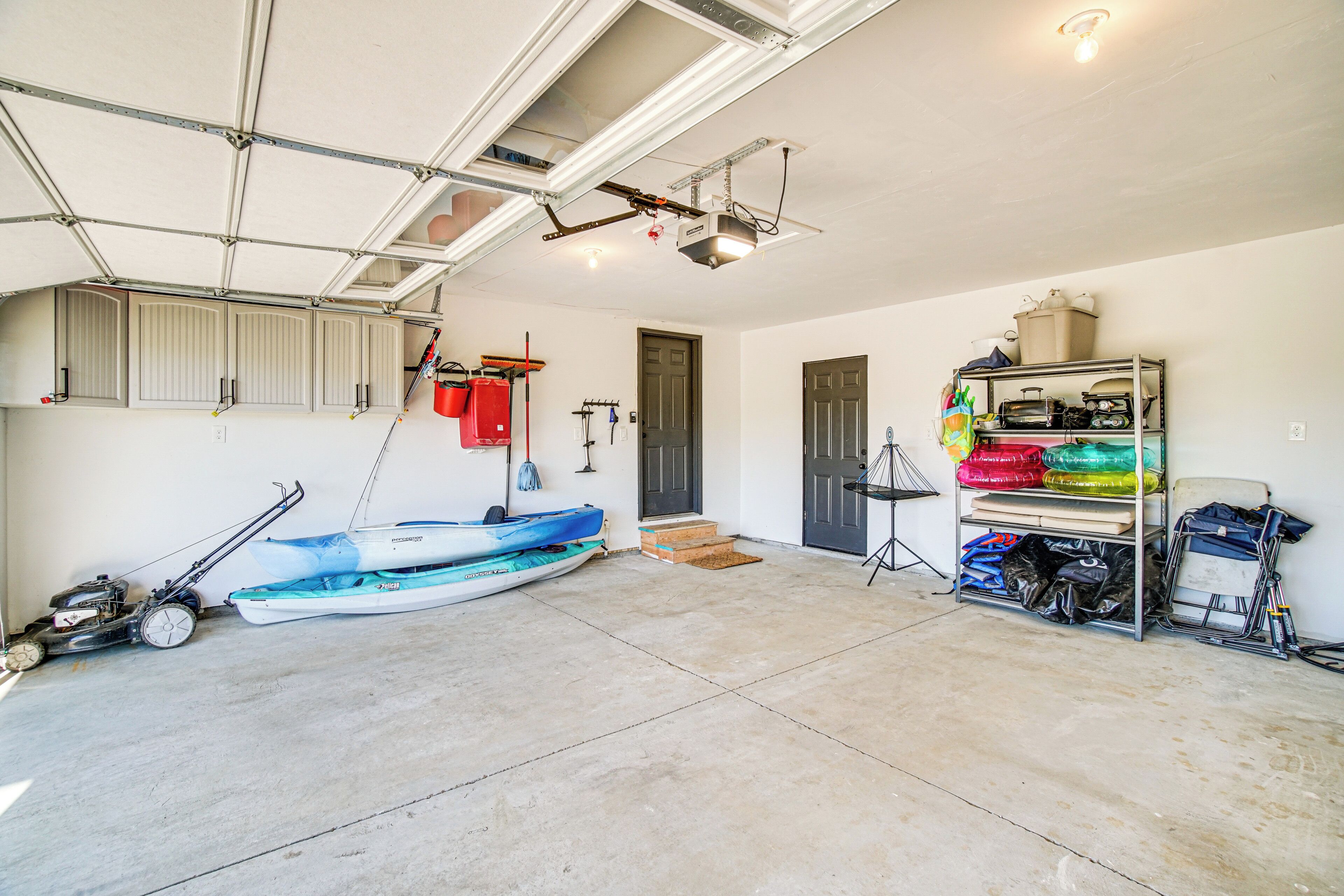 A garage with a kayak, a lawnmower, and a shelving unit with various items.