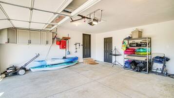 A garage with a kayak, a lawnmower, and a shelving unit with various items.