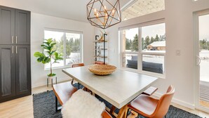 Een moderne eetruimte met een grote tafel, stoelen, een geometrische hanglamp en uitzicht op het buitengebied.