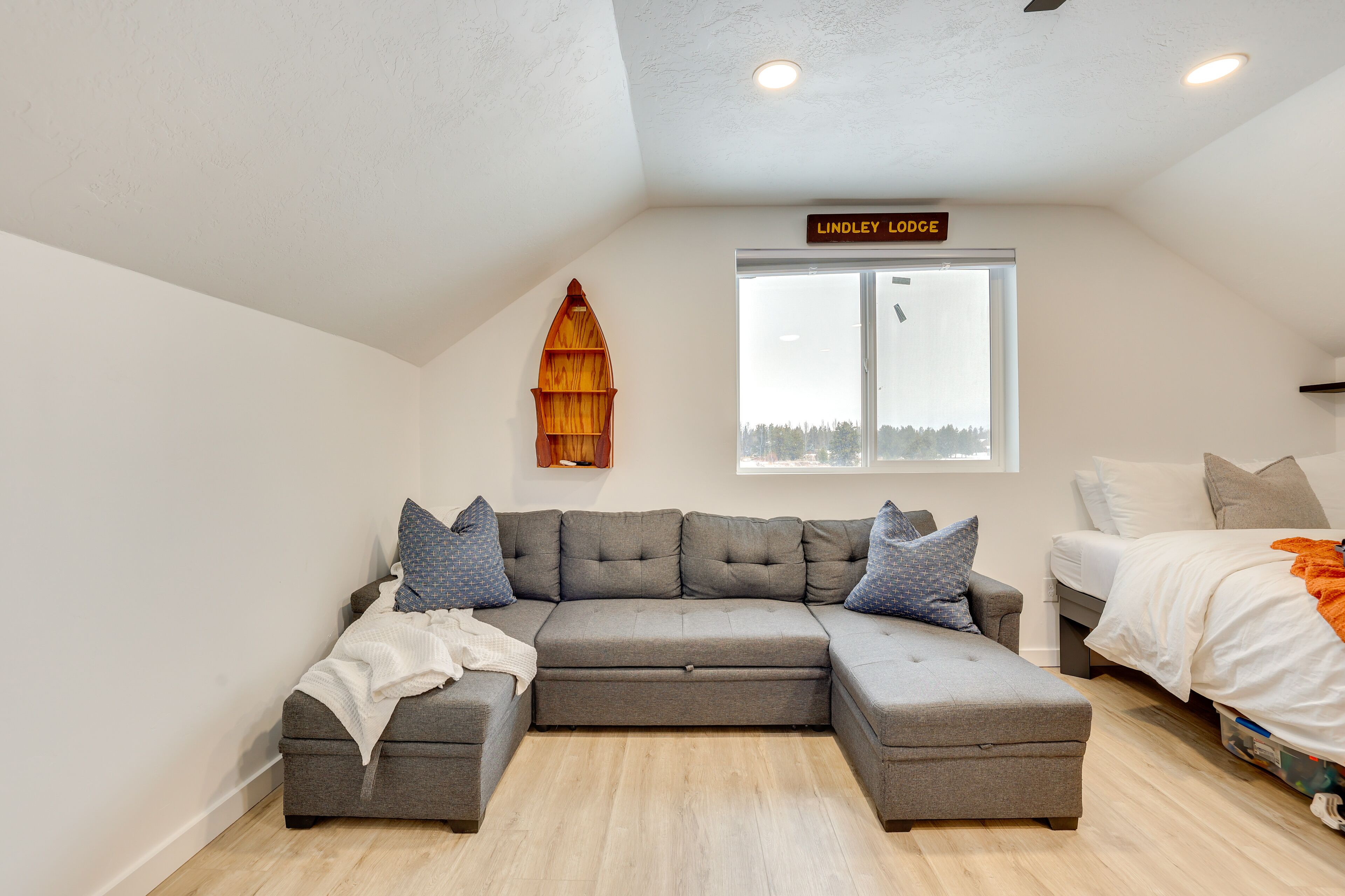 A modern loft bedroom with a gray sectional sofa, a bed, and a lofted window.