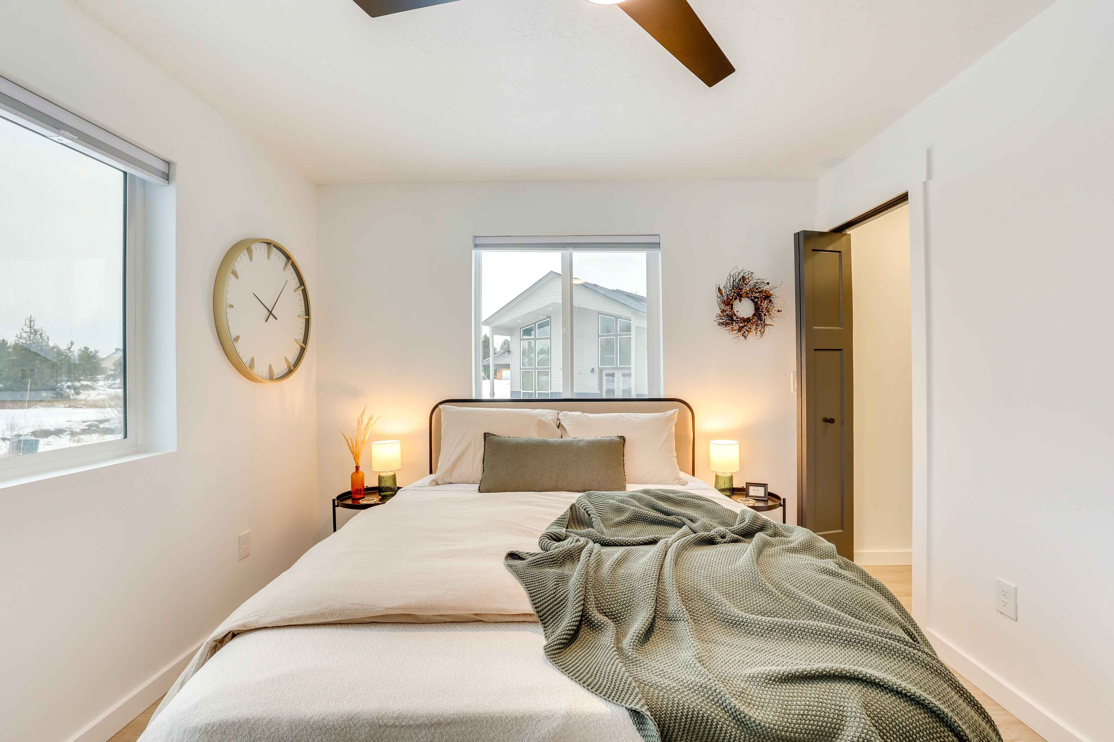 Un dormitorio con cama, lámparas de noche, un reloj de pared, una ventana y una puerta.